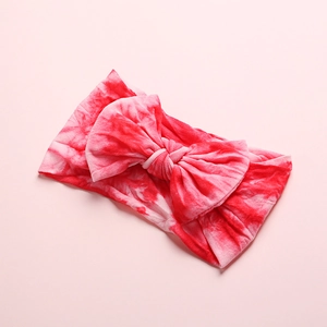 Detailed close-up of a red and white tie-dye baby headband featuring a large soft bow