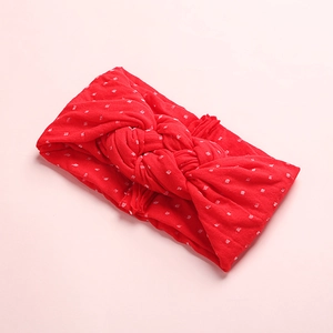 Détail d'un bandeau en nylon rouge à pois blancs avec un nœud torsadé pour bébé