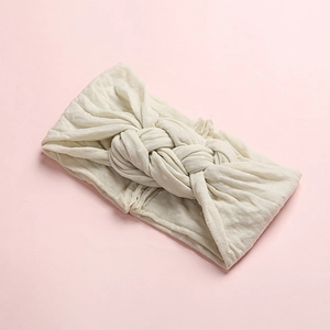 Vue détaillée d'un bandeau pour bébé en tricot blanc crème avec un design à nœud torsadé