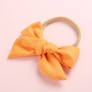 Close-up of soft orange cotton windmill bow headband for infants on a pink background