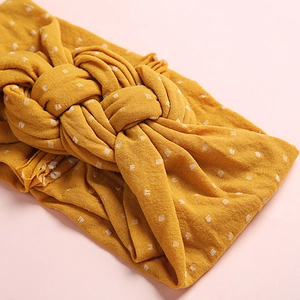 Gros plan du bandeau en nylon jaune à nœud avec pois blancs et texture de tricot fin