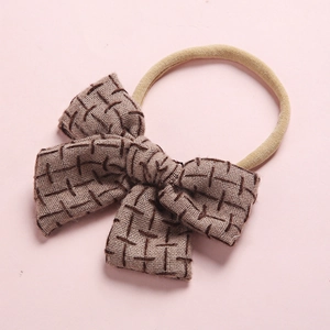 Detail of baby linen hairband with brown bow featuring dark cross-stitch embroidery