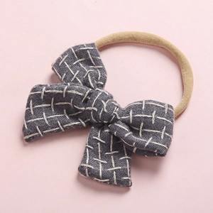 Close-up of baby hair band featuring a dusty blue linen-style bow with white cross-stitching