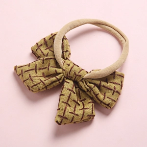 Detail of mustard yellow linen baby bow with red cross-stitch on elastic nylon headband