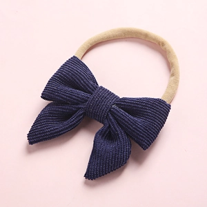 Detail of navy blue corduroy bow on soft beige nylon headband for babies