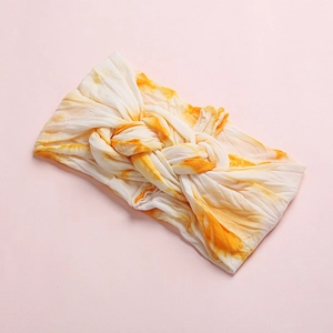 Close-up of baby tie-dye headband with soft orange and white fabric and center knot detail