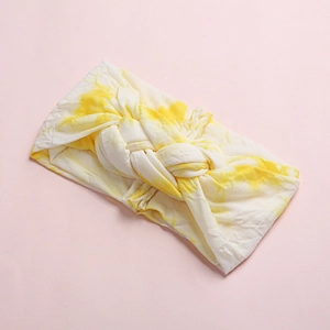 Macro detail of tie-dye baby headband showing soft yellow knit texture and braided knot