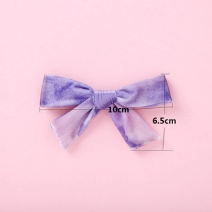 Détail d'un nœud à cheveux en velours violet, dimensions 10cm x 6,5cm sur fond rose