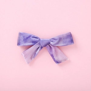 Détail d'un nœud à cheveux en velours violet avec rubans sur un fond rose poudré