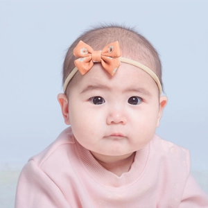 Cute baby headband featuring an orange floral bow on a thin nude elastic band for infants