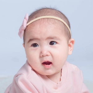 Close-up of baby girl wearing a pale pink satin bow headband on a soft blue background