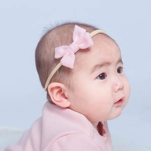 Detail view of a soft pink fabric bow headband worn by an infant with elastic band