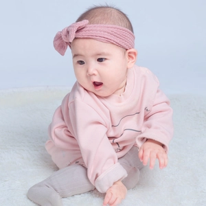 Détail du bandeau tricoté rose pour bébé avec nœud et body en coton à manches longues