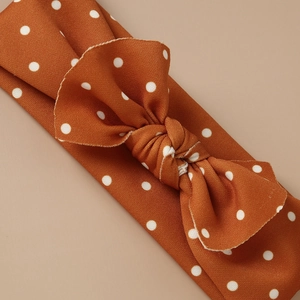 Elastic baby headband in burnt orange with white polka dots and twisted bow design