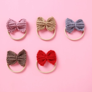 Close-up of five colorful knitted bow headbands for babies on a soft pink background