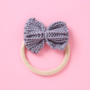 Detail of hand-knitted gray woolen bow attached to a beige elastic high-stretch hair tie