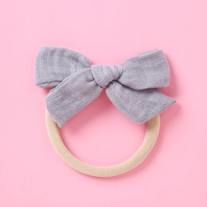 Détail du bandeau bébé avec nœud gris et élastique en nylon doux sur fond rose