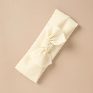 Detailed close-up of cream knit baby headband featuring a large soft textured bow accent