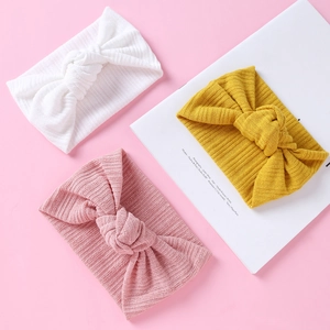 Draufsicht auf weiche Rippstrick-Babystirnbänder in Weiß, Gelb und Rosa mit Knotenschleife
