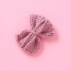 Pink knitted bow hair clip with ribbed texture for girls on soft pink background