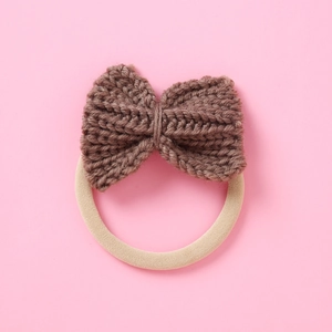 Close-up of handmade dark brown knitted bow hair tie with cream elastic band