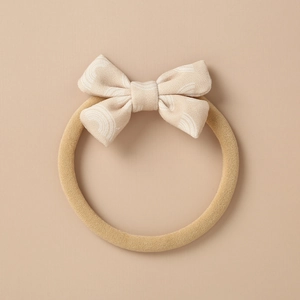Close-up of soft beige baby headband featuring a bow with white rainbow patterns
