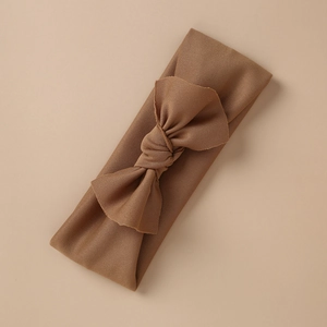 Detail shot of a tan stretch knit baby headband with a handmade bow on a beige background