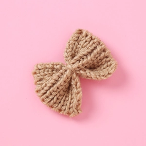 Detail of khaki crochet knit bow hair clip with intricate woven texture on pink background