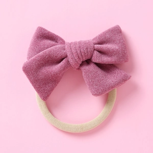 Détail d'un nœud en daim rose foncé attaché à un bandeau élastique en nylon beige doux