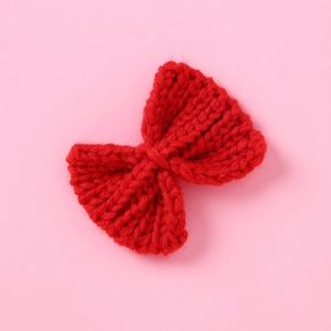 Close-up of a red knitted yarn bow hair clip with detailed ribbed texture on pink paper