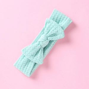 Gros plan sur la texture gaufrée vert menthe d'un bandeau pour bébé avec nœud sur fond rose