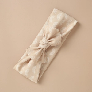 Detail of beige elastic baby headband with bow and white rainbow print pattern