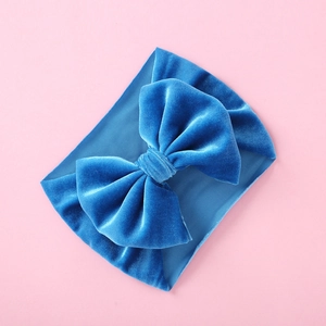 Detail of blue velvet bow and textured elastic band on baby headband set on pink backdrop