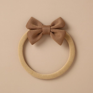 Detail of baby headband with brown bow and beige ribbed knit fabric texture