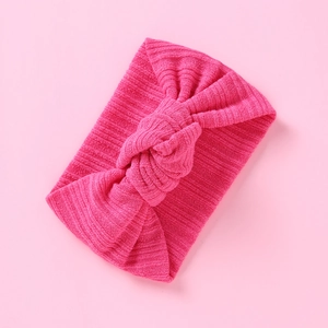 Hellrosa geripptes Strick-Babystirnband mit Knoten auf sanft rosa Hintergrund