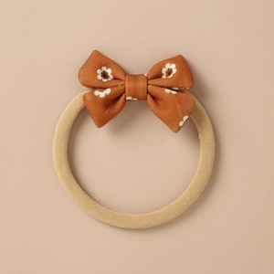 Detail of soft knitted baby headband with a brown daisy bow in vintage floral style