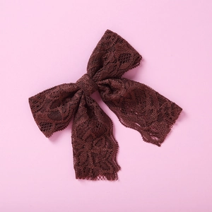 Detail der dunkelbraunen Spitzen-Haarschleife mit Rosenmuster auf rosa Hintergrund