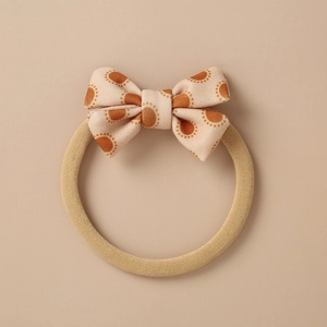 Close-up of beige vintage bow hair tie with orange polka dots and elastic band