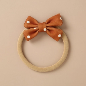 Close-up of caramel fabric bow with white polka dots on a seamless nylon baby headband