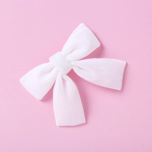 Vue détaillée d'une barrette à nœud en velours blanc doux sur fond rose pastel