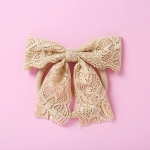 Détail du bandeau en dentelle champagne avec nœud floral sur fond rose doux
