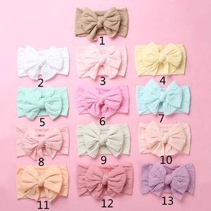 Collection of 13 colorful soft nylon baby headbands with large bows on a pink background