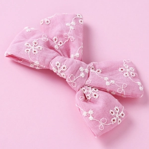 Close-up of pink cotton hair clip with intricate white floral embroidery and cutout details
