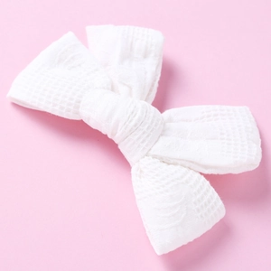 Detail shot of white waffle textured cotton bow hair clip on a soft pink background