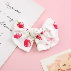 Detailed close-up of a cotton hair bow with cherry and polka dot print on pink background