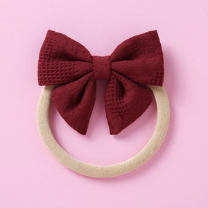Détail d'un bandeau bébé avec un nœud à carreaux rouge foncé sur bande nylon