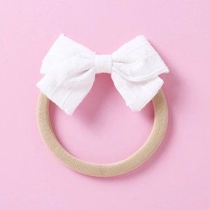 Detailed texture of white jacquard bow on soft beige nylon elastic headband for infants