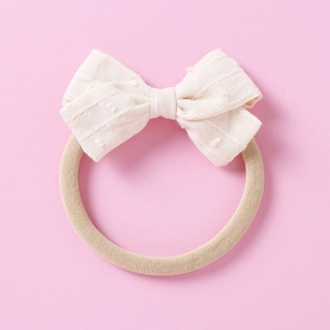 Close-up of the cream Swiss Dot jacquard bow and soft nylon headband for infants