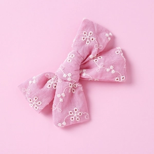 Detail view of pink cotton bow hair clip with intricate white floral embroidery and texture
