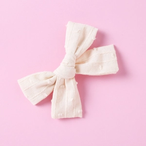 Detailed close-up of cream white cotton bow hair clip with textured polka dot fabric